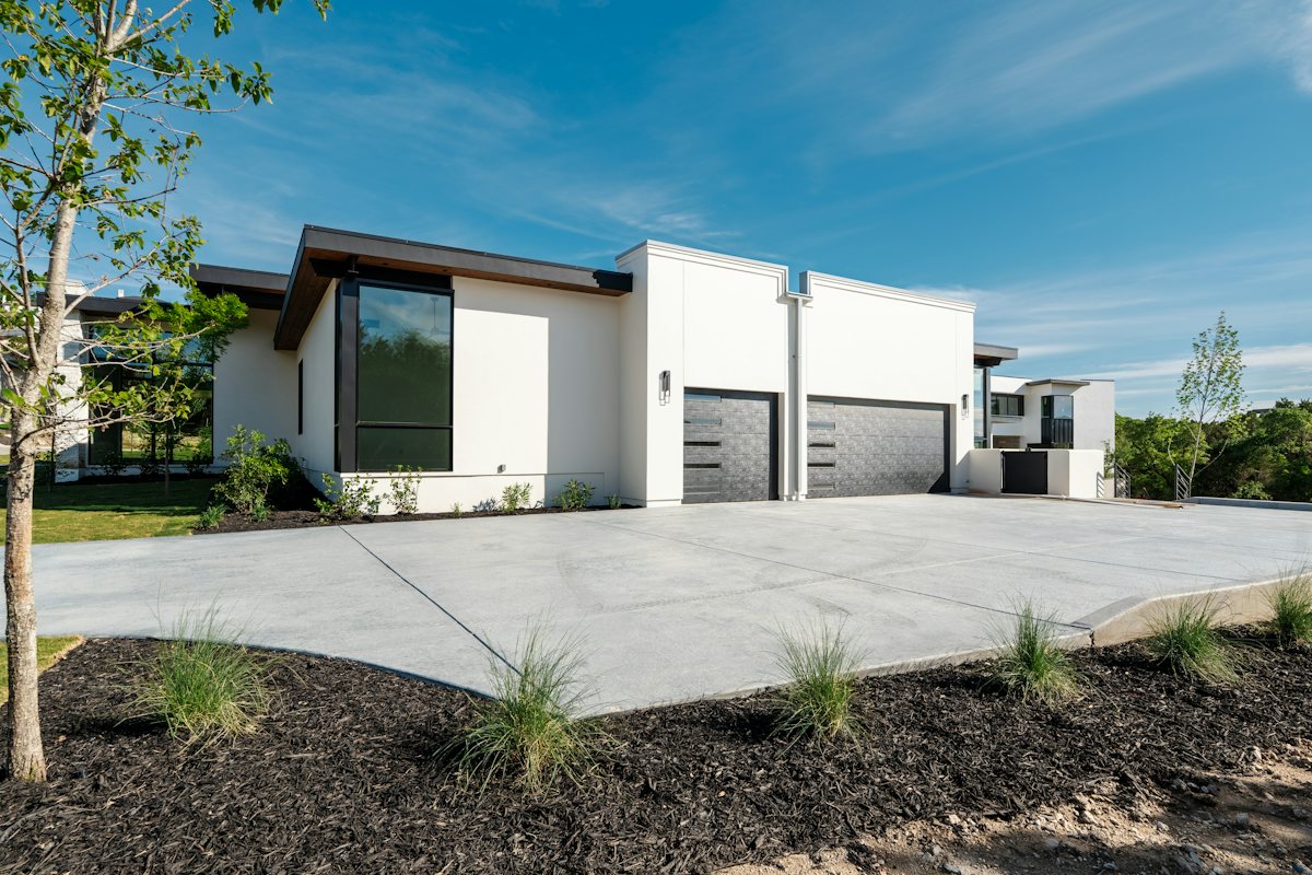 Wide concrete driveway leading to a white house with two garage doors